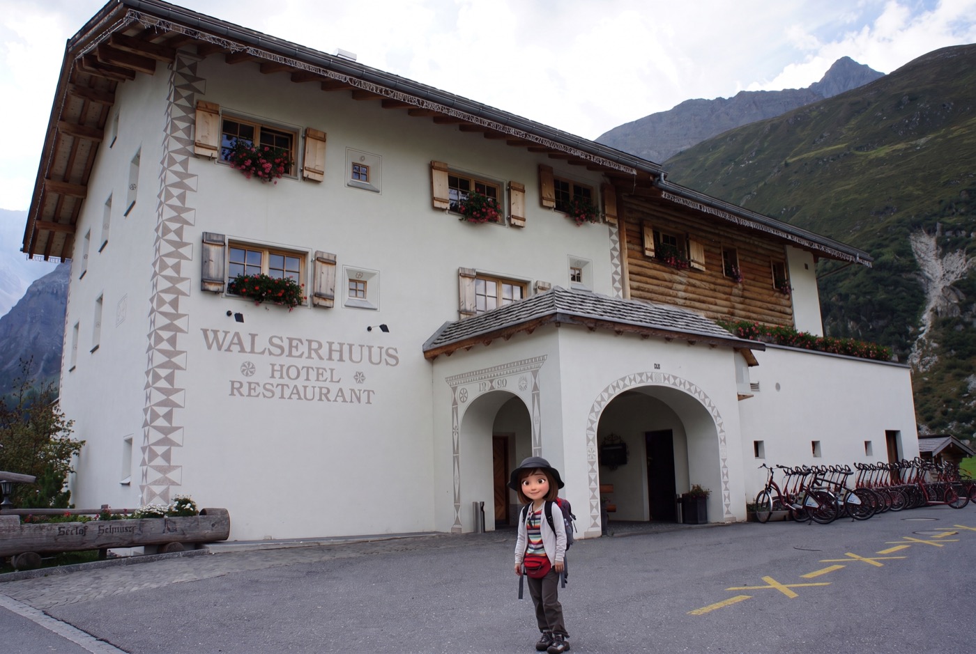 ヴァルザーフースの正面。白い壁に灰色のスグラフィート装飾、窓辺には赤い花。「WALSERHUUS HOTEL RESTAURANT」の文字と
