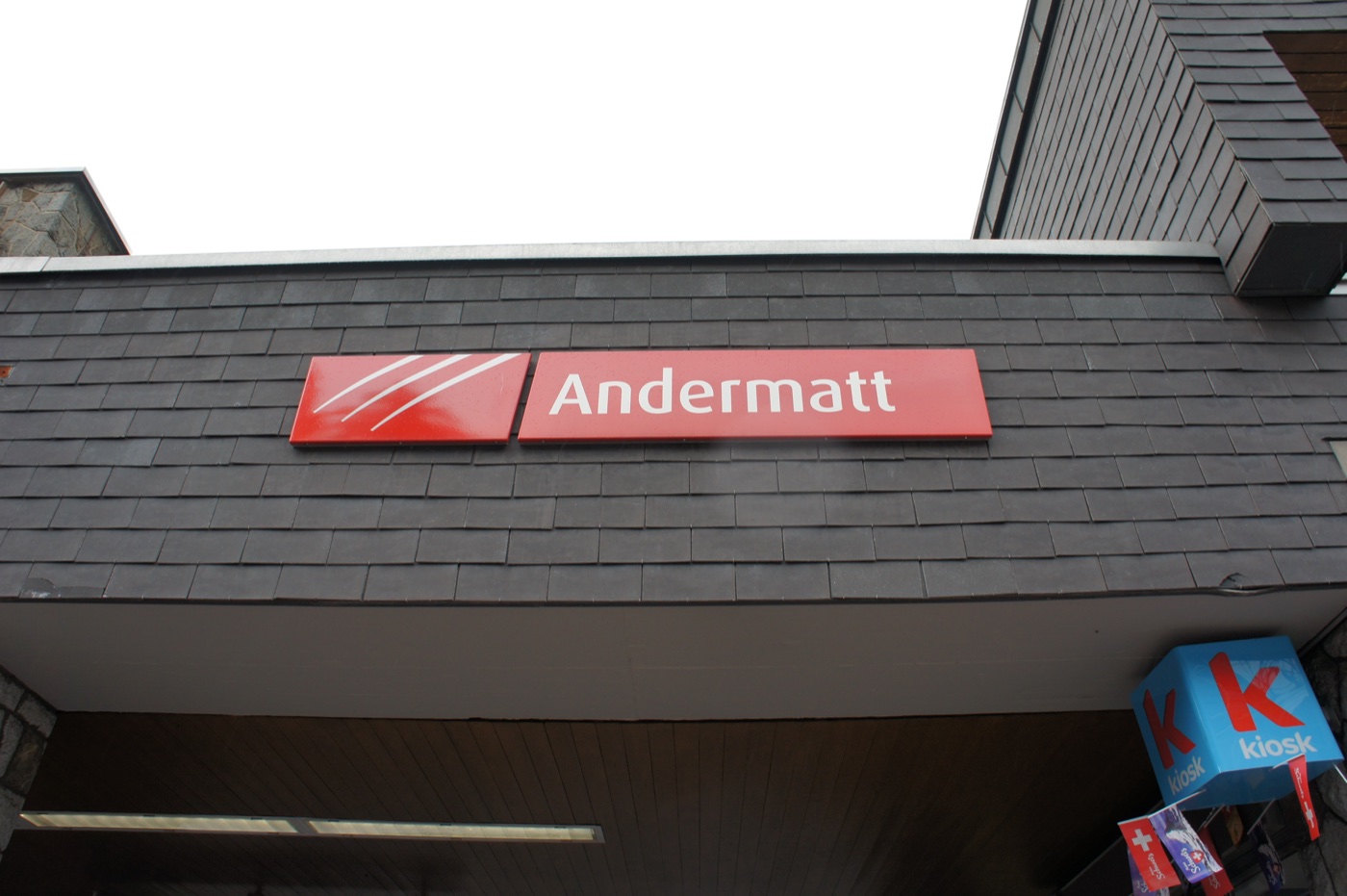 長い列車移動のすえ、夜になってゴッタルド峠の麓の町アンダーマット(Andermatt)に到着。駅の赤い看板と、売店(kiosk)。外はすっか